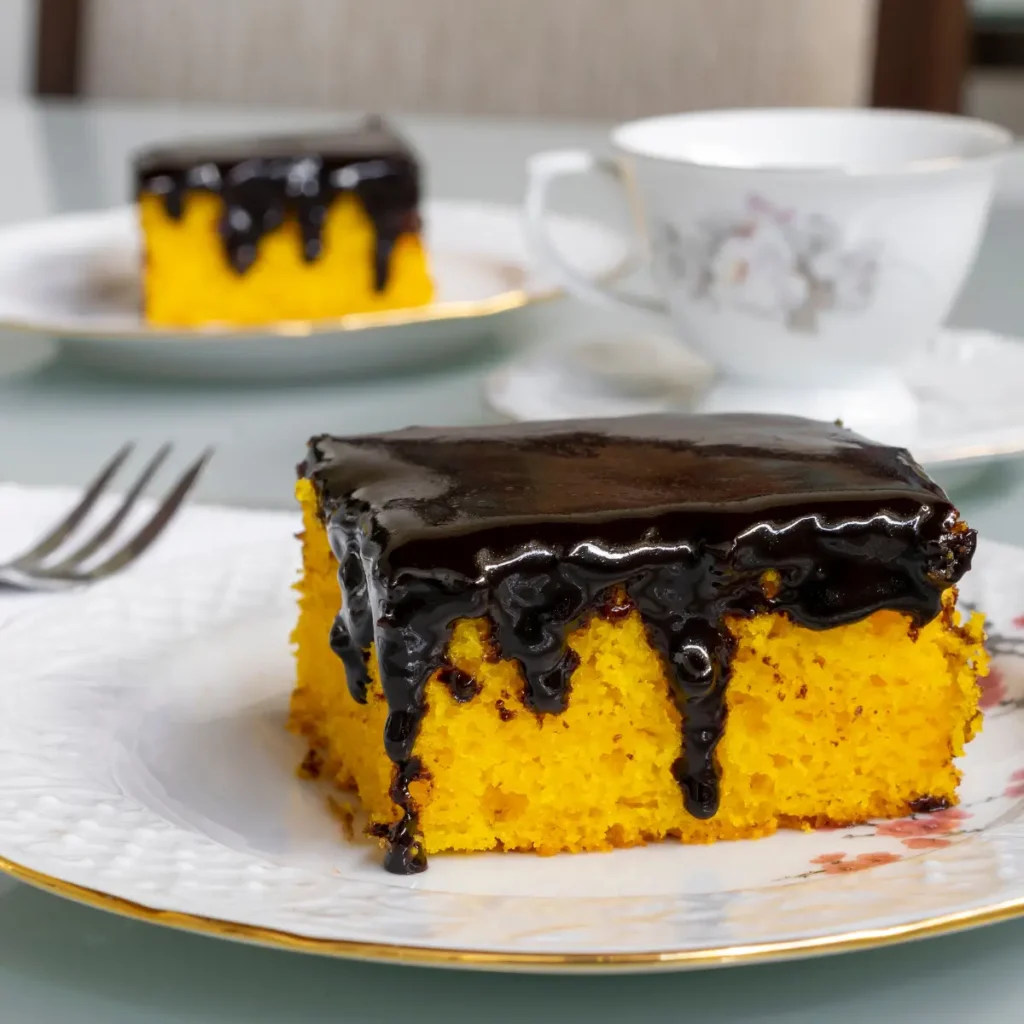 Fatia de bolo de cenoura com calda de chocolate em prato branco.