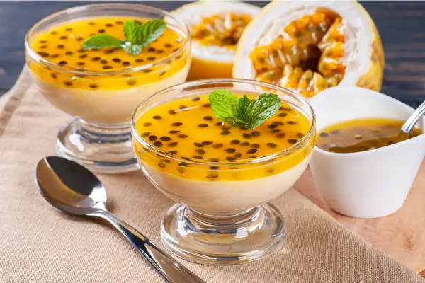 taça de vidro com mousse de maracujá e sementes de maracujá em cima, com uma colher ao lado.