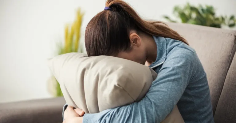 Mulher triste com a cabeça apoiada em um travesseiro no sofá, demonstrando cansaço emocional.