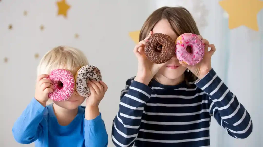 Duas crianças brincando com donuts como se fossem óculos, em um momento divertido de atividades educativas em casa.