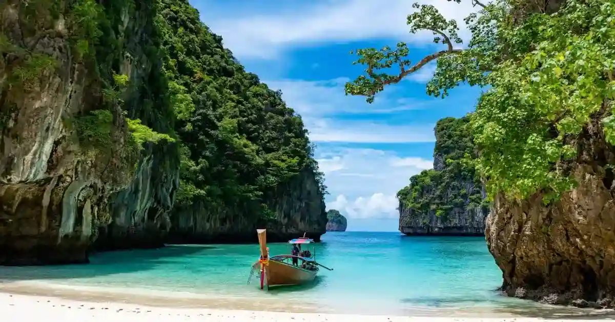 Barco ancorado em uma praia de areia branca entre ilhas privadas com águas cristalinas e vegetação tropical.
