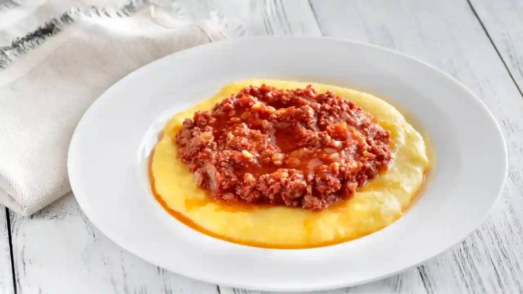 Polenta cremosa com molho de carne servida como sugestão de jantar por 10 reais em prato branco sobre mesa rústica.