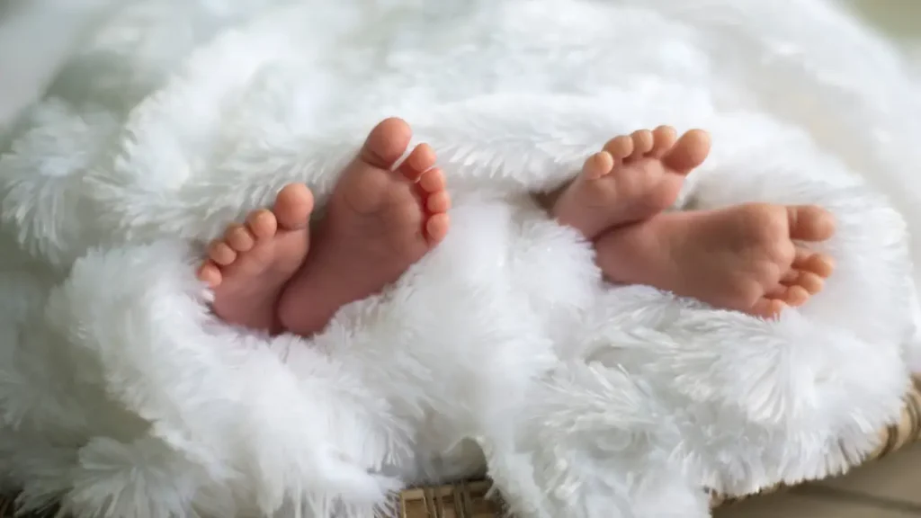Pés pequenos de bebê envoltos em cobertor branco e fofo; imagem inspiradora para escolher nomes para gêmeos que celebrem a ternura e o aconchego dos primeiros dias de vida.