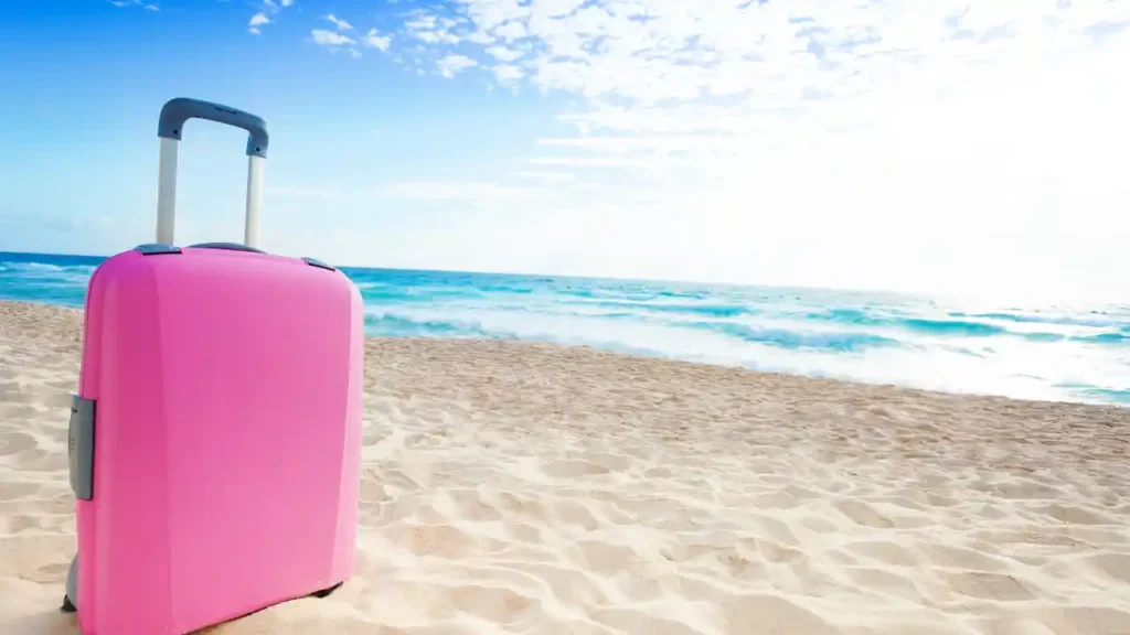 Mala rosa em pé na areia de uma praia ensolarada — inspiração visual sobre o que levar na mala para passar 7 dias no litoral.
