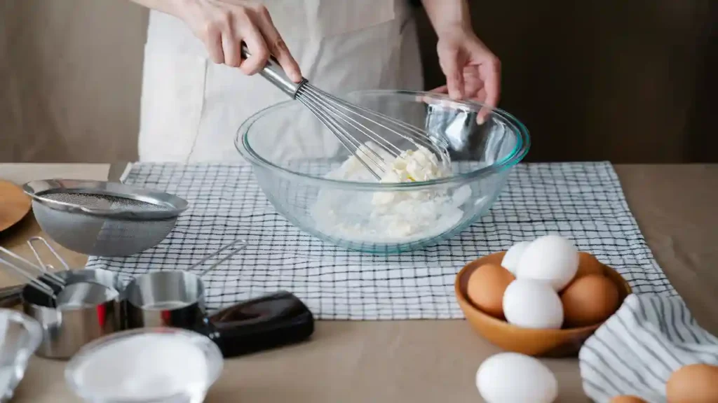 Pessoa misturando ingredientes em tigela de vidro, cercada por utensílios de cozinha, ilustrando receitas com 3 ingredientes de forma simples e caseira.