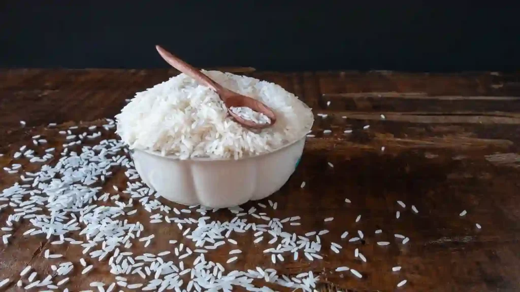 Tigela branca com arroz cru e colher de madeira sobre superfície rústica, ideal para ilustrar receitas com sobra de arroz.