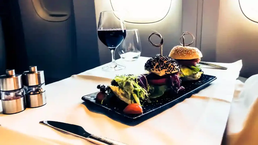 Hambúrgueres servidos com vinho tinto em bandeja de avião, ilustrando refeição antecipada durante o voo.