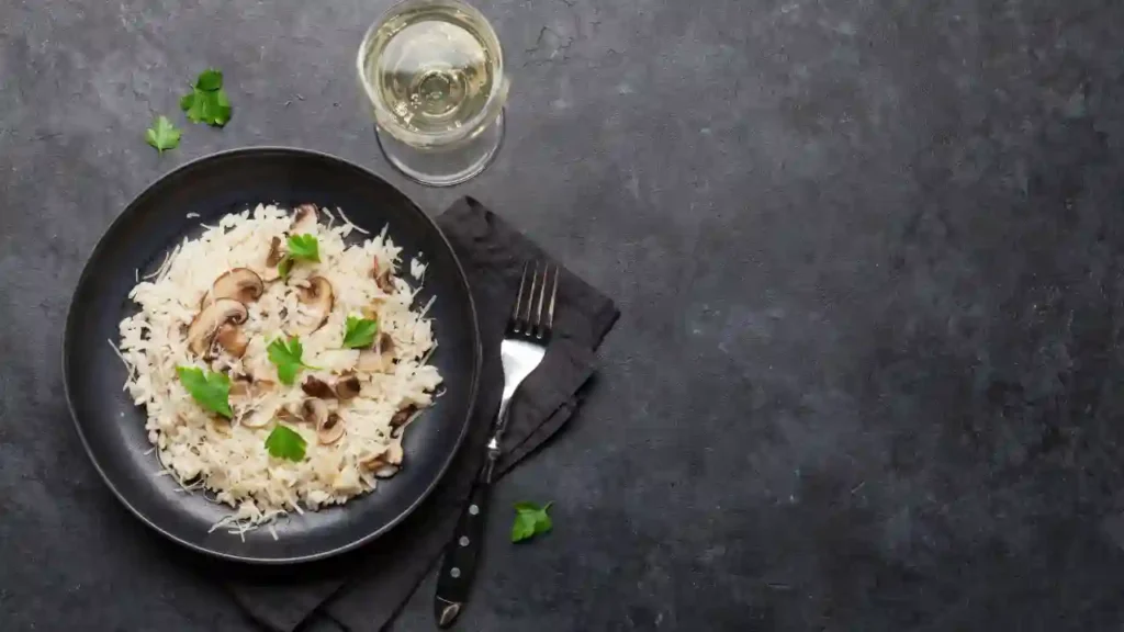 Prato de risoto com cogumelos servido com vinho branco, ilustrando uma refeição antecipada sofisticada.