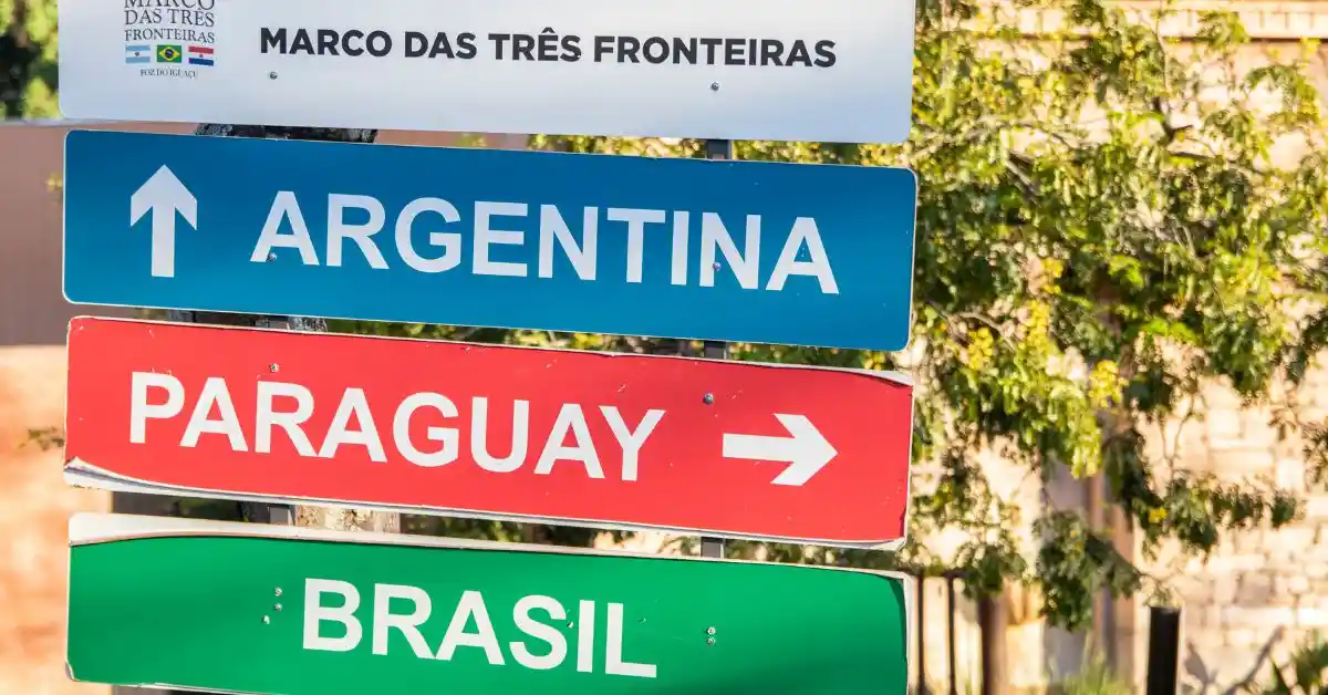 Claro, aqui está a versão ajustada sem o hífen: - Alt text: Viagens que atravessam fronteiras a pé – Placa direcional no Marco das Três Fronteiras indicando os caminhos para Argentina, Paraguai e Brasil.