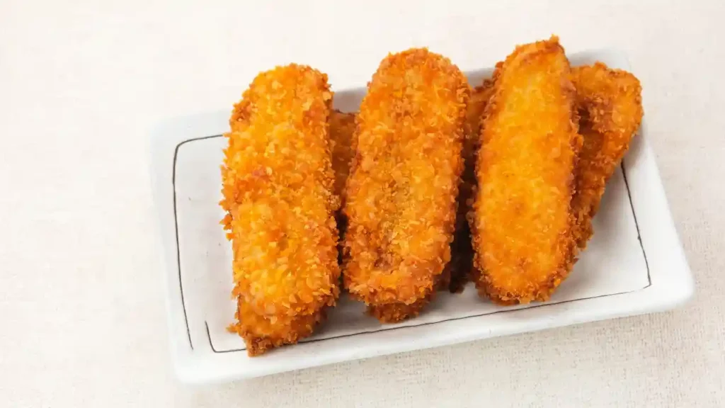 Croquetes dourados e empanados servidos em prato branco sobre superfície clara, destacando a textura crocante em estilo semelhante à banana frita crocante.