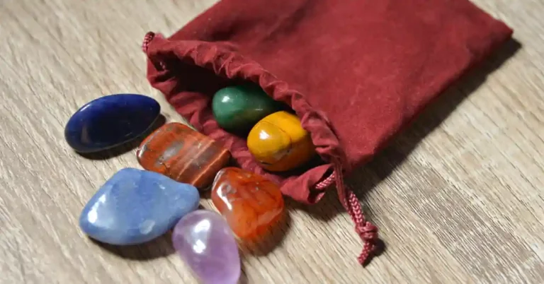 Cristais coloridos que potencializam a proteção espiritual espalhados sobre uma superfície de madeira, saindo de uma pequena bolsa vermelha de veludo.