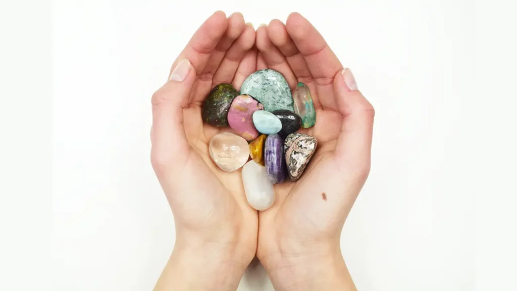 Mãos segurando cristais polidos de várias cores e formas, representando cristais que potencializam a proteção espiritual com beleza e energia vibrante.
