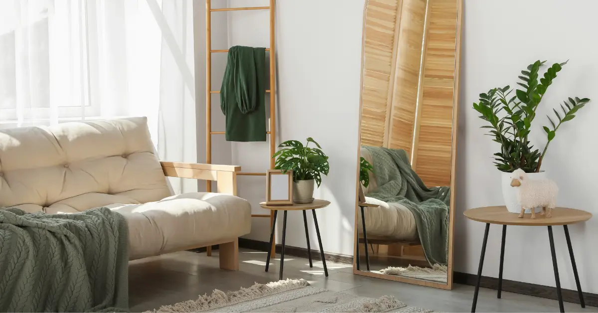 Espelho grande com moldura dourada refletindo planta decorativa em sala para decorar apartamento pequeno