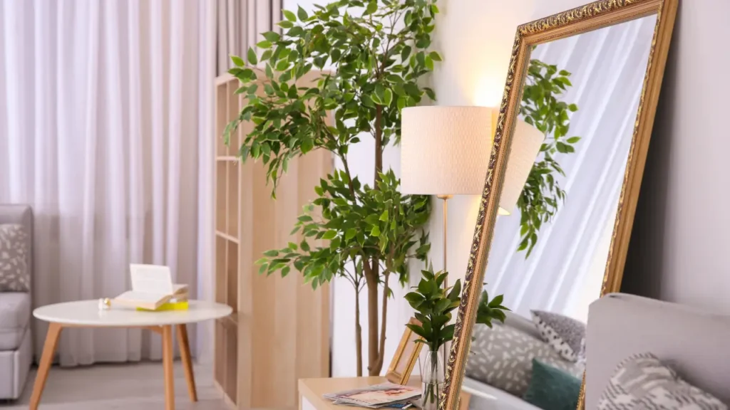 Sala com sofá bege, espelho de corpo inteiro e plantas decorativas para decorar apartamento pequeno