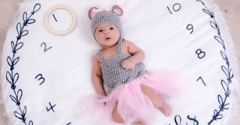 Bebê vestido de rato cinza com saia de tule rosa, deitado sobre um cobertor branco com números bordados de 1 a 12, representando uma das fotos criativas de bebês para registrar o crescimento mensal.