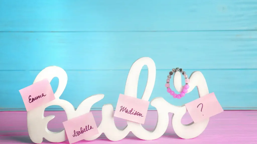 Objeto decorativo com a palavra "Baby", cercado por notas adesivas com nomes como Emma, Isabella e Madison, representando escolhas afetivas e nomes com significado forte.