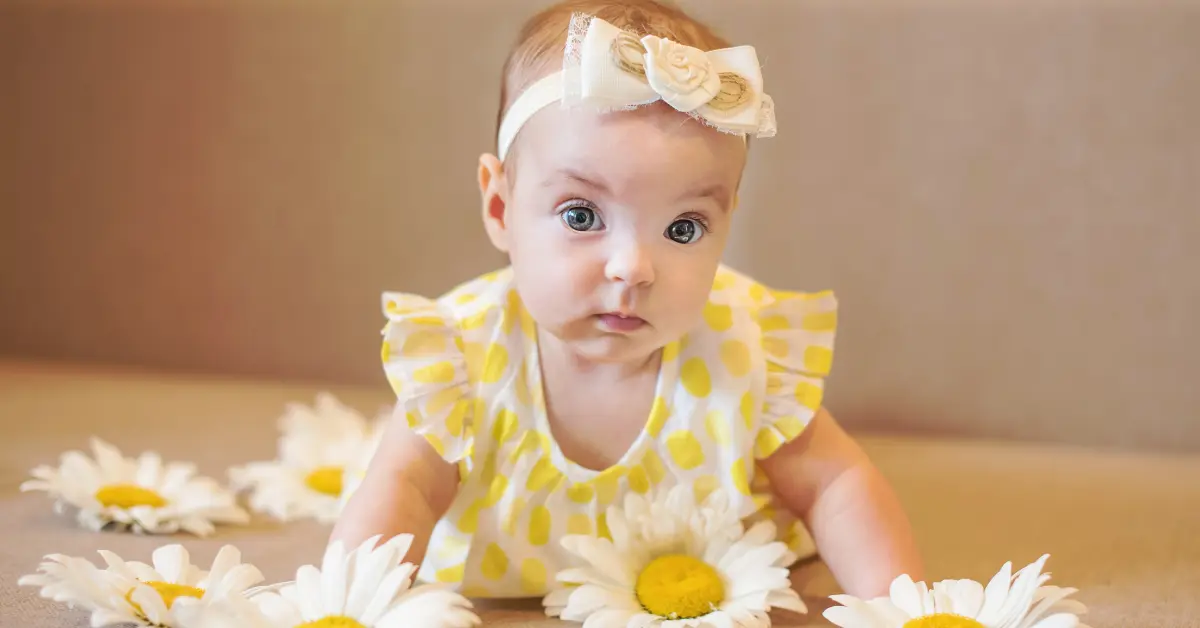 Bebê com vestido amarelo de bolinhas e faixa com flor entre margaridas brancas; imagem doce que inspira nomes naturais raros com toque floral e sensibilidade.