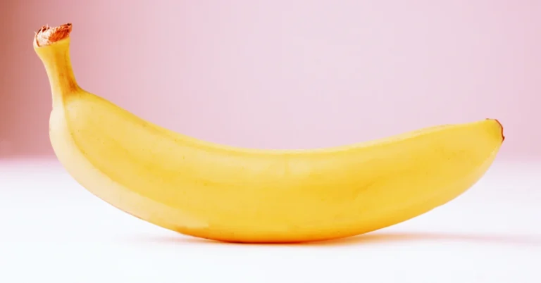 Banana madura e curvada sobre fundo rosa vibrante, representando o ingrediente principal do pastel de banana.
