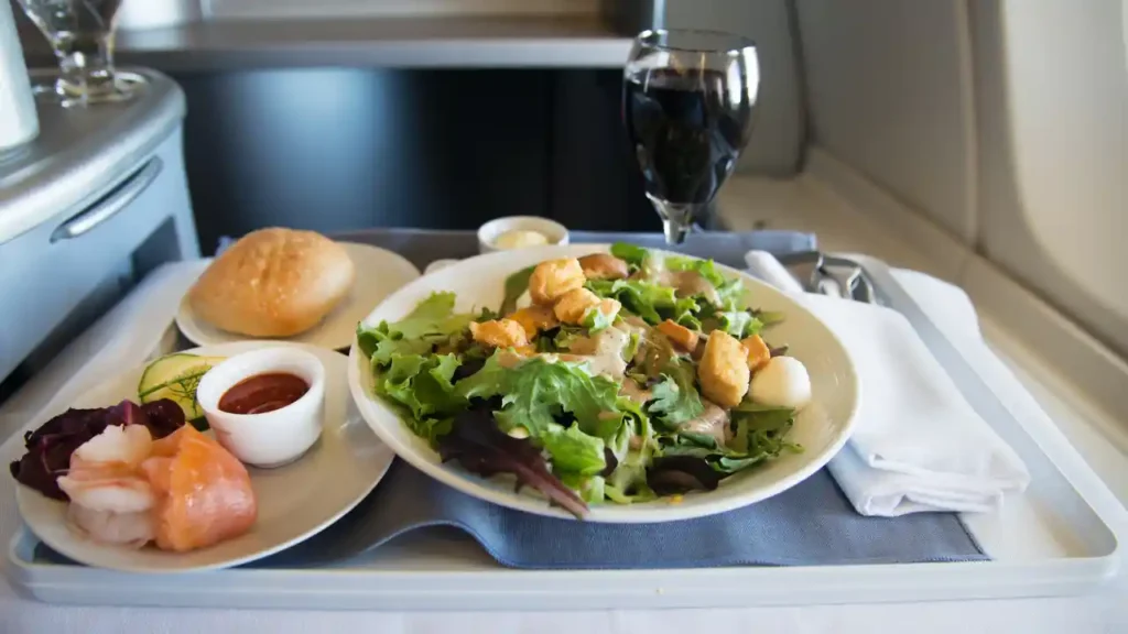 Bandeja de refeição antecipada no voo com salada, frutos do mar, pão e vinho tinto em mesa de avião.