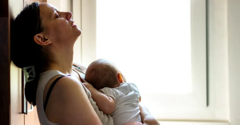 Pessoa segura um bebê adormecido no colo, sentada perto de uma janela, em um momento de tranquilidade que simboliza o sono do bebê.