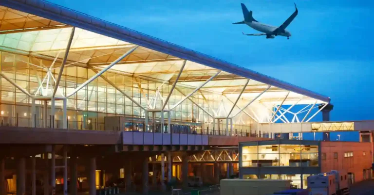 Terminal de aeroporto moderno ao entardecer com avião no céu, representando o fluxo de voos internacionais.