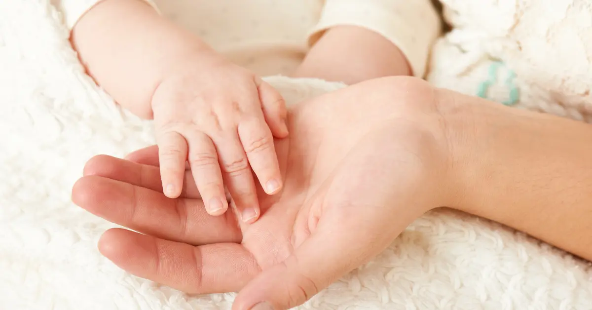 Mão de bebê repousando suavemente sobre a mão de um adulto, simbolizando cuidado e vínculo — uma representação sensível de a verdade por trás da maternidade.