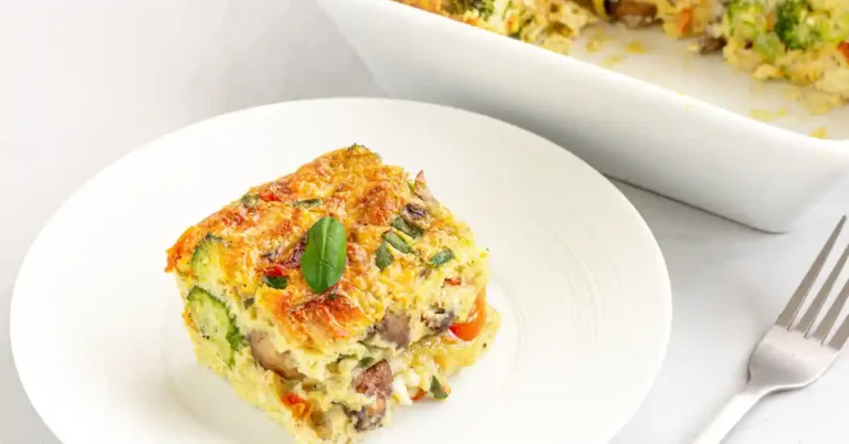 Porção de arroz cremoso de forno com frango servida em prato branco, com vegetais visíveis e folha de manjericão como decoração.