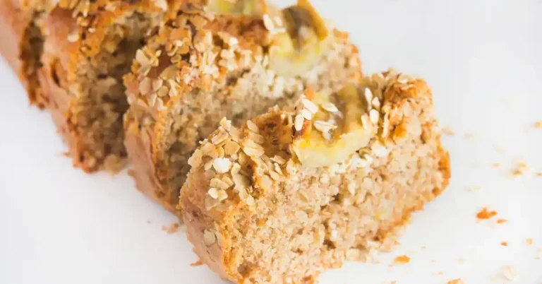 Fatia de bolo de banana com aveia sem açúcar, com textura úmida e cobertura de banana e flocos de aveia sobre fundo claro.