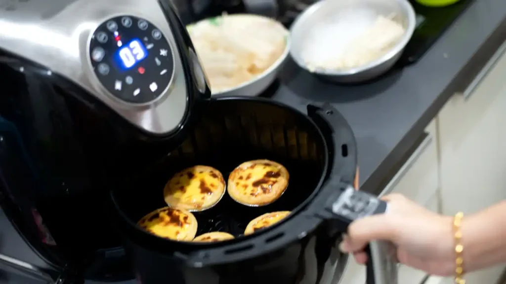 Air fryer preta com cinco tortinhas assadas no cesto e visor digital mostrando três minutos restantes — preparo de café da manhã fit na Air fryer.