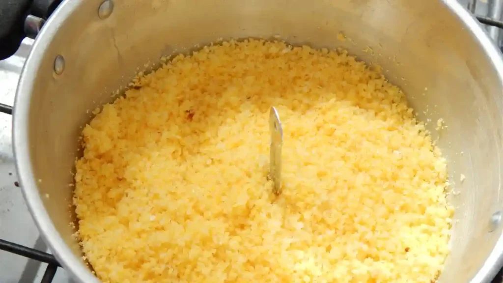 Panela com cuscuz fit colorido recém-cozido, de textura fofa e tom amarelo vibrante, com utensílio metálico ao centro.