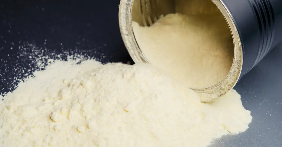 Leite em pó derramado de uma lata metálica sobre uma superfície escura, ingrediente essencial para preparar doce gelado com leite em pó.