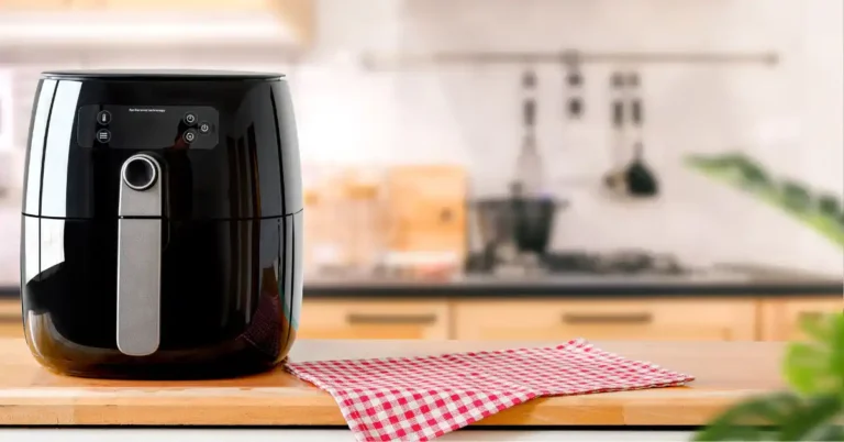 Air fryer preta sobre uma bancada de madeira com um pano xadrez vermelho e branco ao lado, em uma cozinha moderna — ideal para preparar frutas na Air fryer.