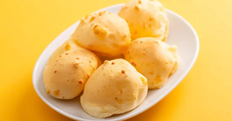 Prato branco com cinco unidades de pão de queijo com creme de leite, sobre fundo amarelo vibrante.