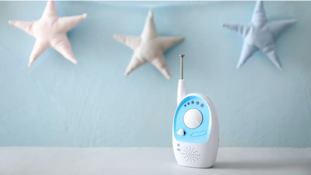 Monitor de bebê branco e azul com antena, posicionado diante de decoração com estrelas, representando produtos inovadores para maternidade voltados à segurança infantil.