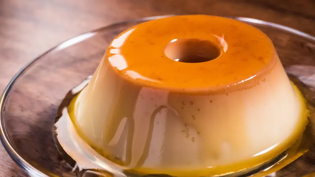 Pudim de leite em pó sem forno servido em prato branco com calda de caramelo, sobre guardanapo amarelo.