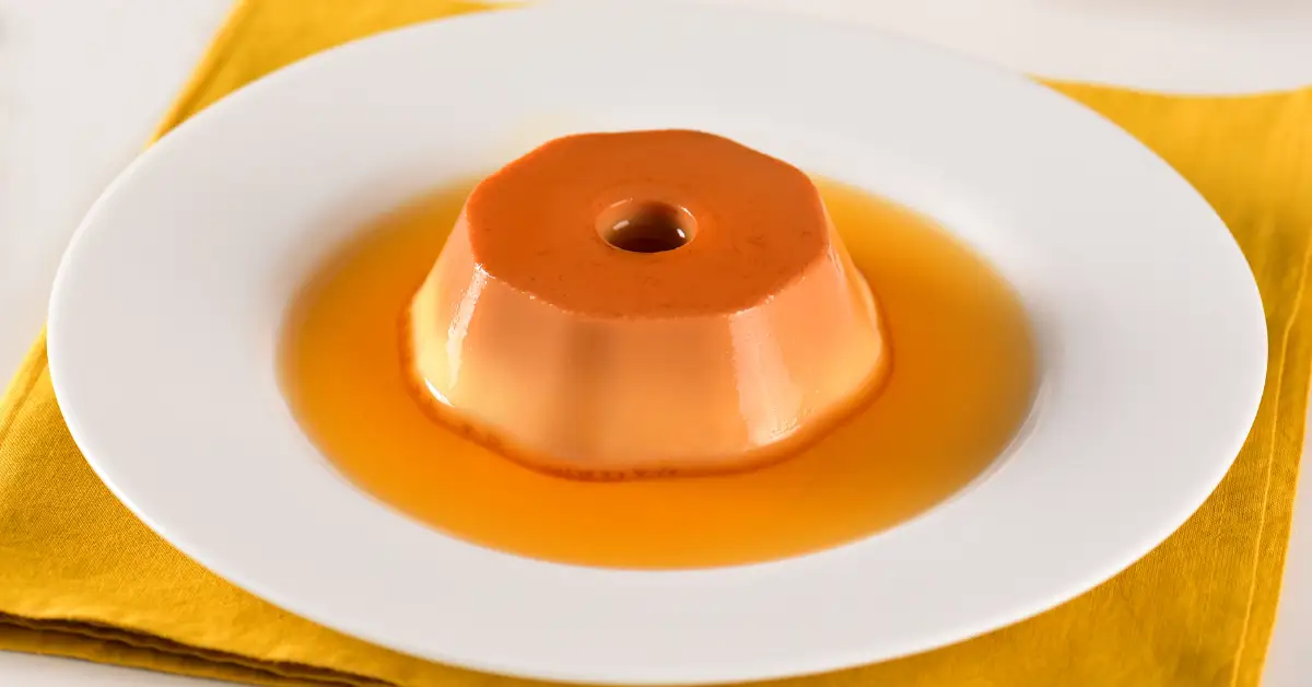 Pudim de leite em pó sem forno servido em prato branco com calda de caramelo, sobre guardanapo amarelo.