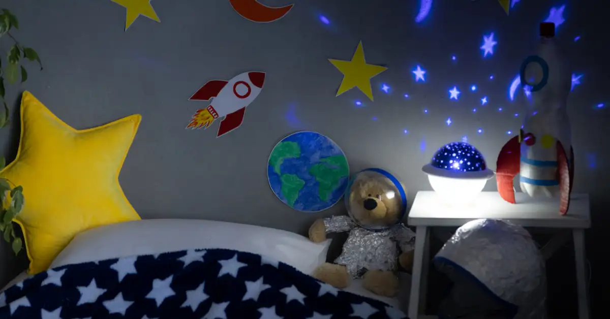 Quarto sensorial para bebê com tema espacial, incluindo almofada de estrela, ursinho astronauta e projetor de luzes.