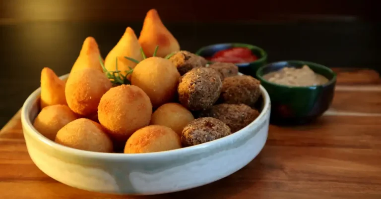 Variedade de salgadinho na air fryer, incluindo coxinhas, bolinhas de queijo e quibes, servidos com molhos em bowl sobre tábua de madeira.