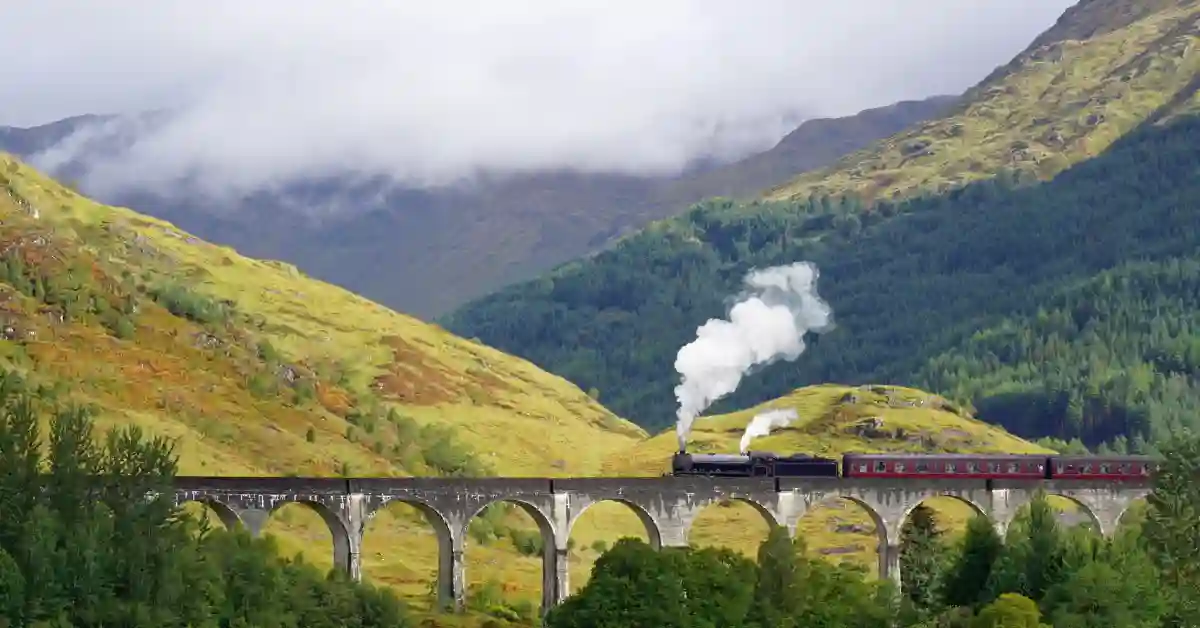 Trem do vinho cruza viaduto de pedra em meio a montanhas verdes e cobertas de névoa, criando um cenário turístico deslumbrante.