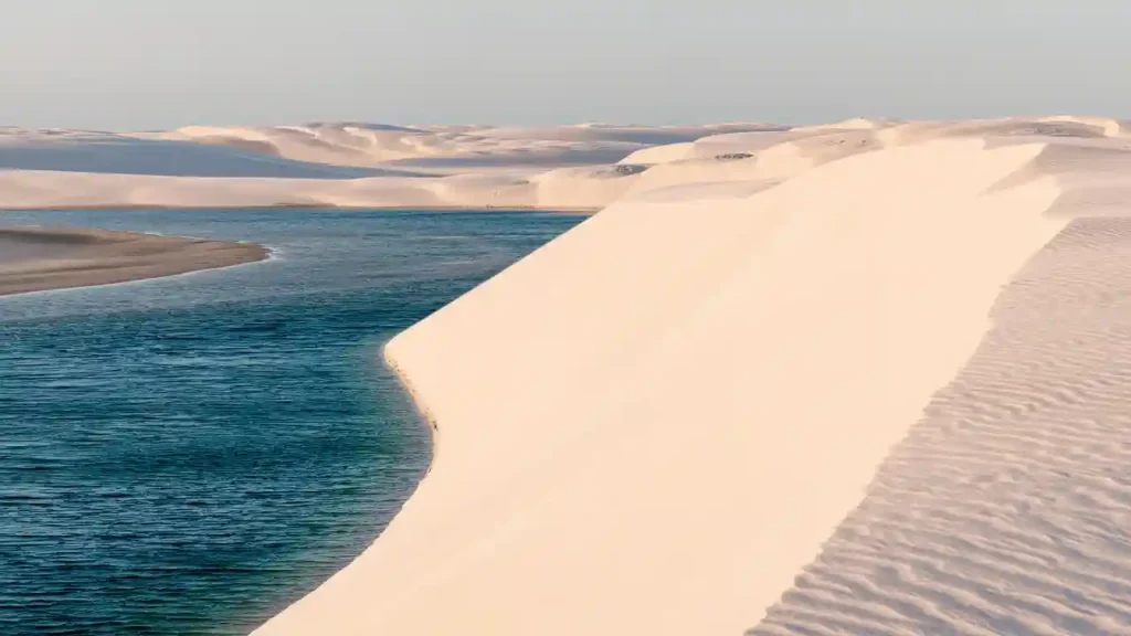 Paisagem de dunas claras ao lado de lagoa azul cristalina — cenário ideal para trilhas para amantes da natureza.