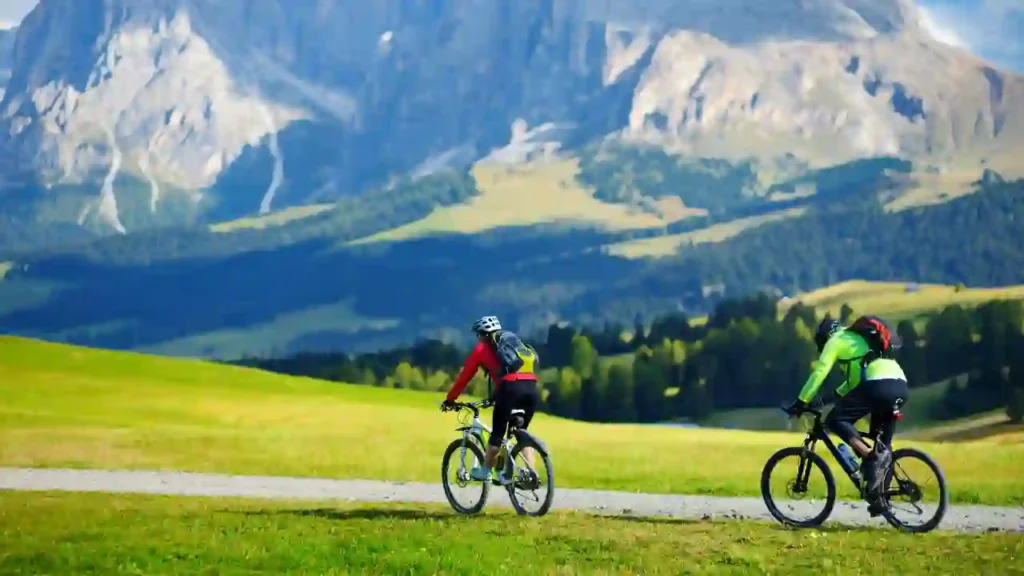 Dois ciclistas percorrem trilha de cascalho em meio a paisagem montanhosa exuberante, representando o ciclismo na Patagônia.
