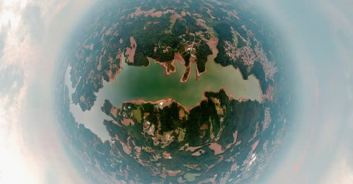 Vista aérea em olho de peixe de uma região com lago rodeado por áreas urbanas e vegetação, representando cidades brasileiras que atraem prosperidade.
