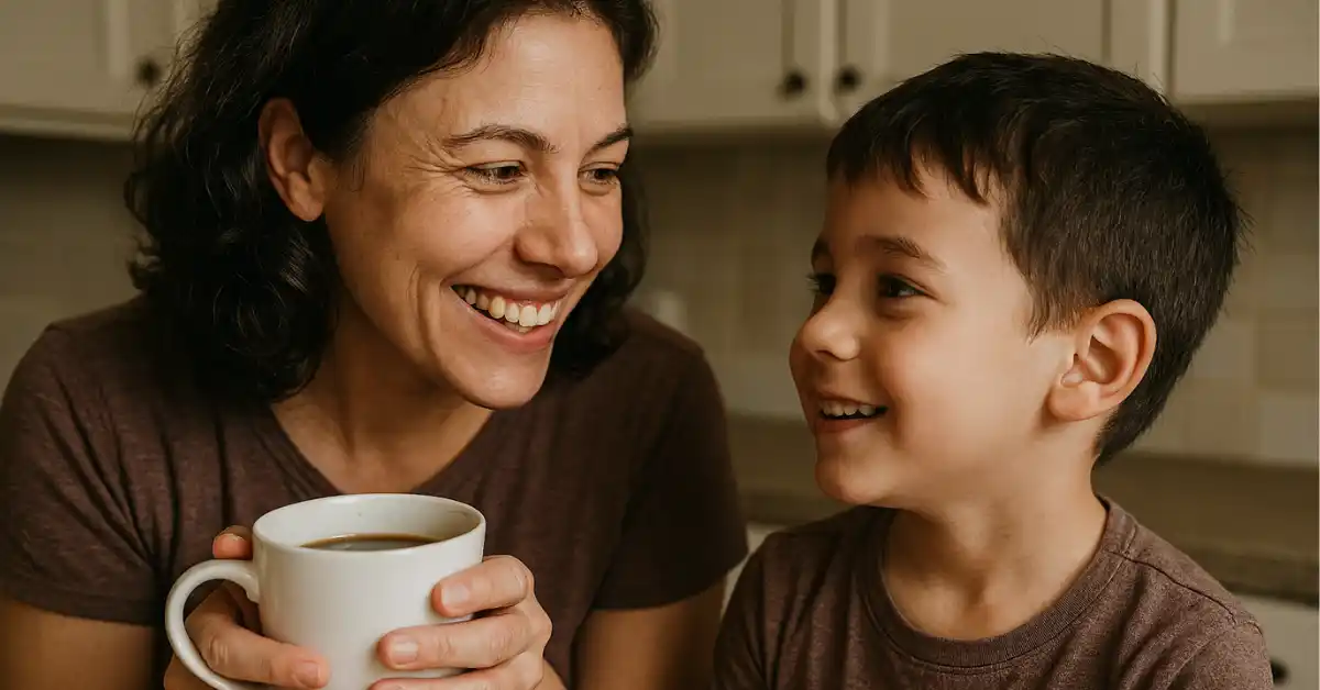 Mãe solo sorridente segurando uma caneca de café enquanto conversa com seu filho pequeno na cozinha, simbolizando os desafios da mãe solo e os momentos de conexão familiar.