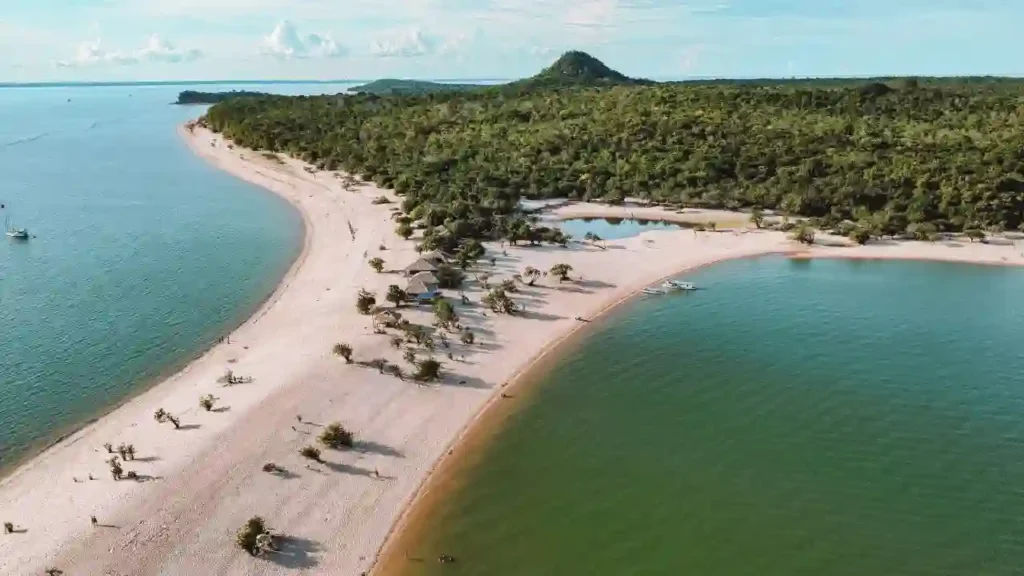 Vista aérea de uma praia de areia branca cercada por floresta tropical e águas calmas, representando destinos brasileiros que unem natureza e bem-estar.