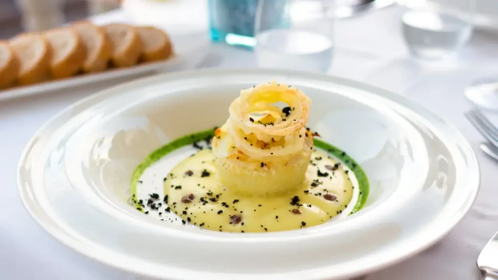 Prato gourmet servido em louça branca sobre toalha de mesa, representando a experiência de bordo refinada.