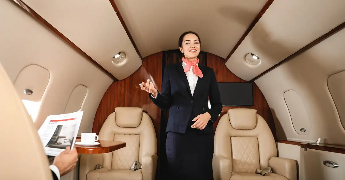 Comissária de bordo sorridente em cabine de avião executivo, destacando a experiência de bordo de alto padrão.