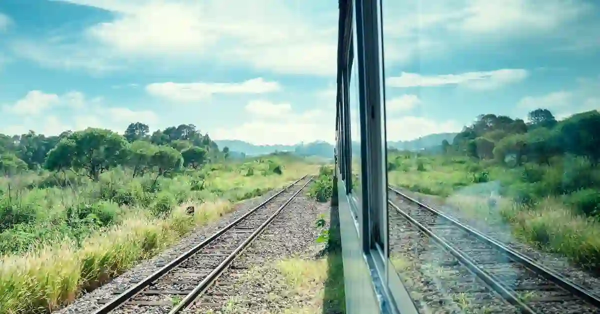 Reflexo da paisagem verde nos trilhos do Expresso Serra Verde visto pela janela do trem em dia parcialmente nublado.