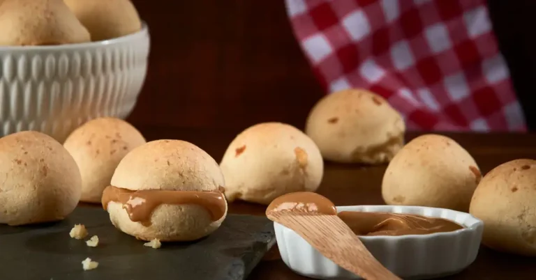 Pão de queijo crocante recheado com doce de leite, servido com creme extra em prato branco e pano xadrez ao fundo.