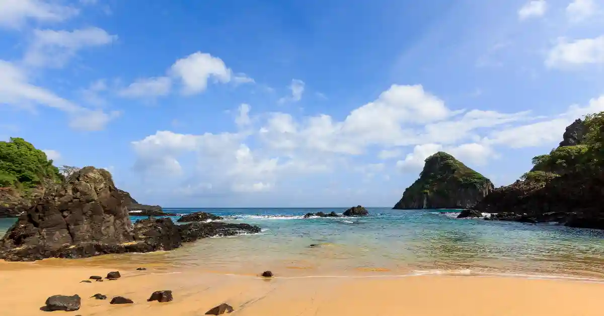 Praia isolada com areia dourada, águas cristalinas e formações rochosas, revelando piscinas naturais secretas no Brasil.