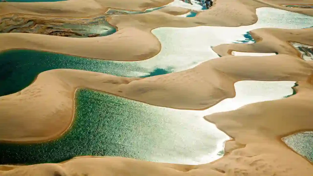 Dunas douradas entrelaçadas com lagoas cristalinas, representando piscinas naturais secretas no Brasil.